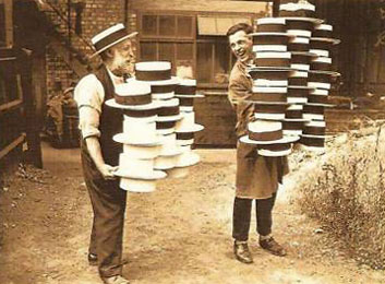Foto: zwei Hutmacher mit einem Stapel Hüte