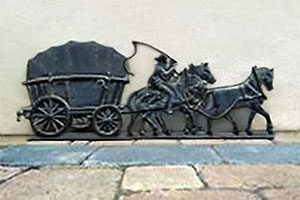 Gußrelief-Bild: Kutsche von drei Pferden gezogen, auf einem davon sitzt die Peitsche schwingend der Kutscher