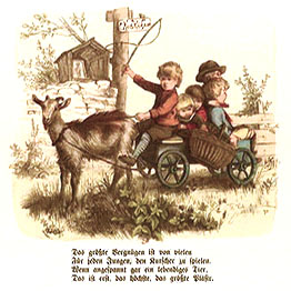 Farbbild: Kinder spielen im Garten Kutschfahrt, Ziege vor Bollerwagen gespannt, auf Brett als Kutschbock ein rot pulloverter Junge mit Peitsche, im Wägelchen vier kleine Kinder eng gedrängt