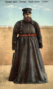 koloriertes Foto: stämmiger, bärtiger, russischer Kutscher in bodenlangem, schwarzblauem Mantel und zylinderartigem Hut, roter Gürtel um den Bauch