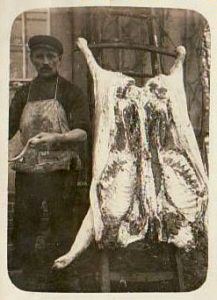 altes Foto: Metzger steht neben aufgeschnittenem und aufgehangenem Schwein