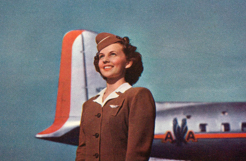 Flugbegleiterin freudig stahlend, jung und schön vor dem Flugzeug stehend