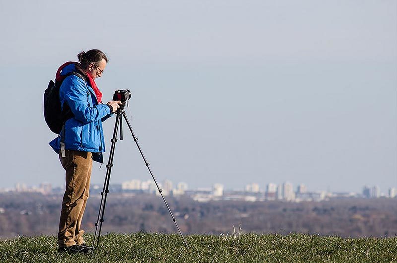 Foto: Fotograf auf einem Hügel mit Kamera auf dem Stativ macht eine Panoramaaufnahme der Stadt