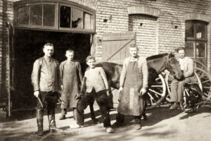 sw-Foto: Hufschied und vier Gesellen lassen sich vor einem Pferd vor der Schmiede, in Pose gebracht, fotografieren