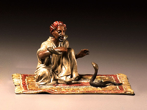 Bronzefigur: dunkelhäutiger Schlangenbeschwörer sitzend auf einem Teppich, auf dem sich vor im eine Schlange empor reckt