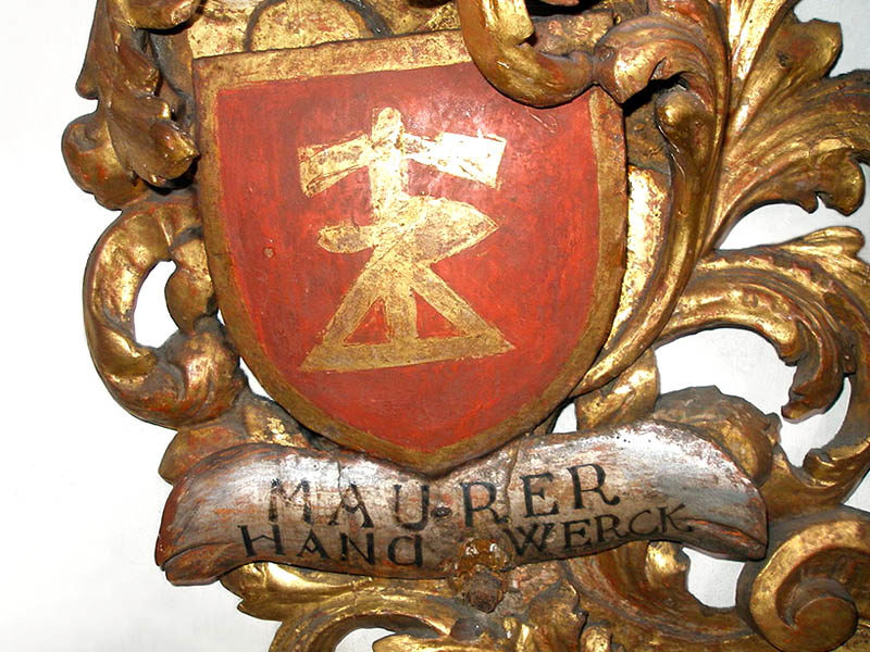 Farbfoto: Schmuckelement, vergoldetes Relief mit rotem Wappen und Aufschrift