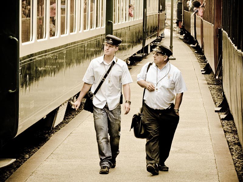 Foto: zwei Schaffner gehen auf einem Bahnsteig zwischen zwei Zügen
