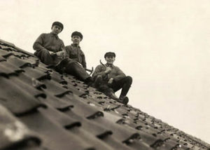 sw-Foto: drei Dachdecker sitzen auf dem fertig gedeckten Dach