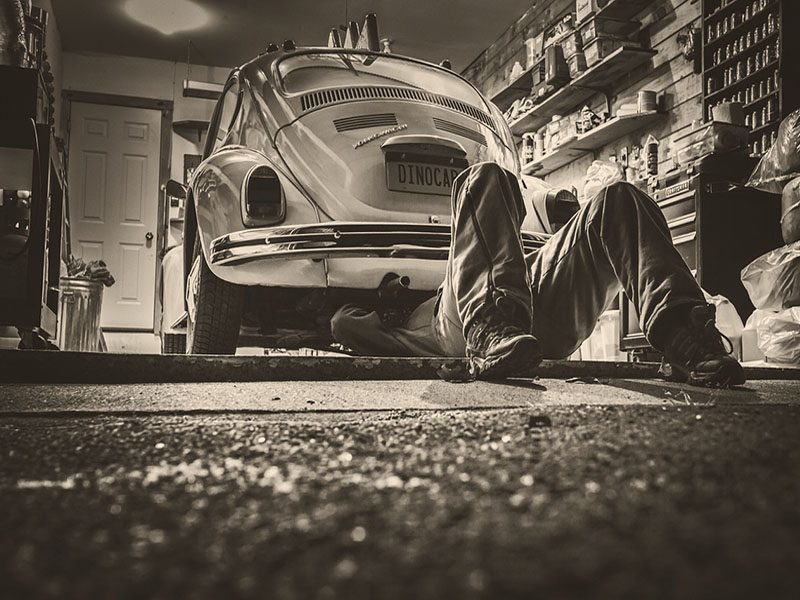 s/w Foto: Autowerkstatt, Mechaniker liegt unter einem VW-Käfer