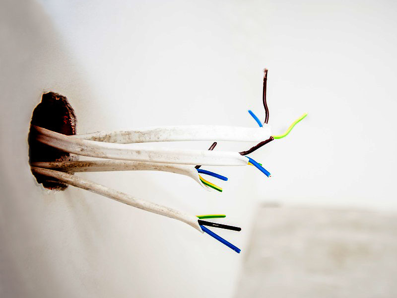Farbfoto: Elektrokabel ragen aus einem Loch in der Wand
