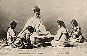sw-Foto: vier Schülerinnen sitzen mit ihrem Lehrer um ein flaches Tischchen auf dem Teppich und haben Bücher aufgeschlagen