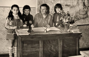 s/w Foto: Lehrerin an einem Sitzpult mit drei Schülerinnen in einem Klassenzimmer