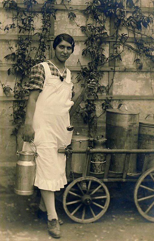 monochromes Foto: junge Frau in Schürze neben Leiterwagen voll Milchgefäßen
