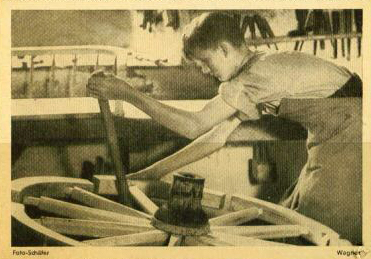 Foto: jugendlicher Handwerker bearbeitet großes Holzrad