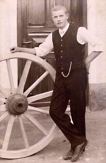 Foto: junger Handwerker steht neben einem Holzrad und stützt sich darauf auf