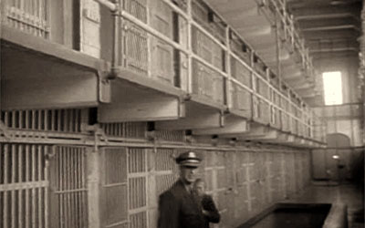 altes sw-Foto: Gefängniswärter im Gang vor Gitter-Zellentüren