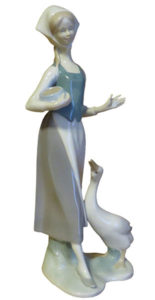 Porzellanfigur: sehr schlanke Gänsemagd mit weißem Kopftuch und blauem Mieder, Futtergefäß im Arm und sich hoch streckende Gans