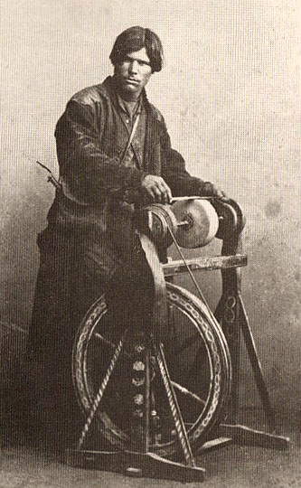 altes s/w Foto: an bockartigem, bäuerlich bemaltem Schleifgerät stehend arbeitender, junger russischer Messerschleifer