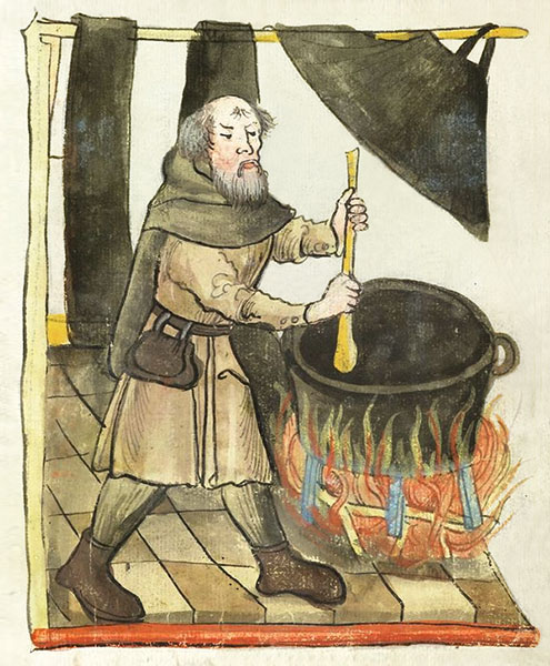 Färber rührt mit Holzstab herum in schwarzem Farbbad in einem Eisenkessel auf einem Gestell, unter dem sich ein Feuer befindet