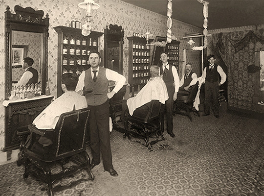 sw Foto: drei Friseure mit vor Spiegeln sitzenden Kunden im Herrensalon -1905