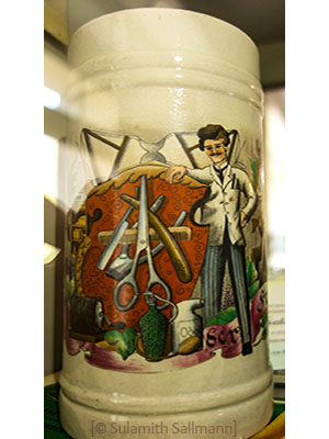 Farbfoto: Keramikhumpen mit Bild eines Friseurs nebst Utensilien