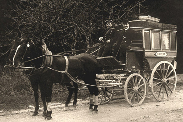 sw Foto: Kutscher und Fahrgast auf dem Kutschbock sitzend bei Fahrt durch den Wald