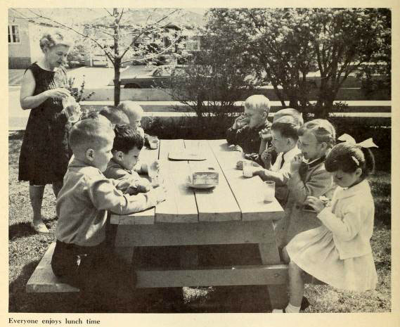 Kindner sitzen im Freien am Tisch und essen ihre Brote