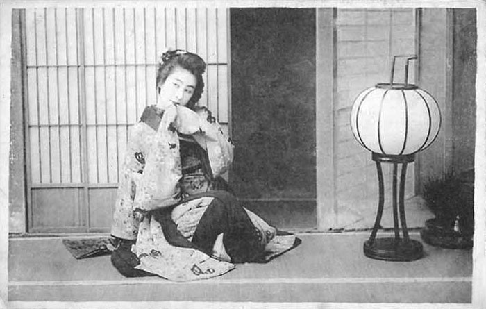 Geisha sitzt auf Boden neben Papierlaterne